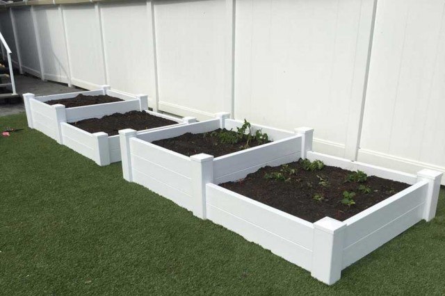 four white planters on lawn filled with soil sitting in front of vinyl fencing