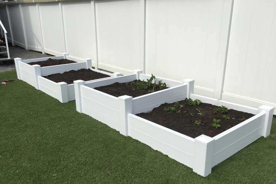 four white planters on lawn filled with soil sitting in front of vinyl fencing