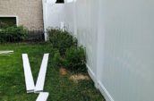 A chain link fence being replaced by a white vinyl fence in a lush green backyard