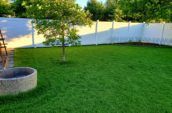 A newly installed white vinyl fence in a lush green backyard