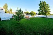 A newly installed white vinyl fence in a lush green backyard